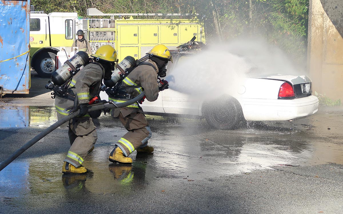 Britt Benn, left, helps demonstrate how to extinguish a car fire as part of celebration activities recognizing the completion of seven weeks of hands-on training at JIBC’s Maple Ridge campus.
