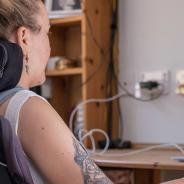 Woman with head in headrest of motorized wheelchair works on laptop.