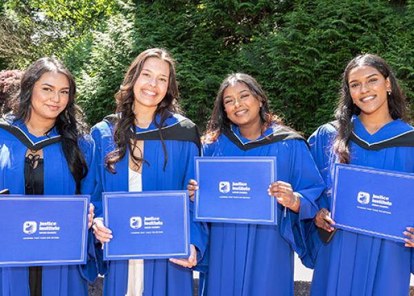 Four women graduates wearing JIBC blue convocation gowns and holding up their certificates.