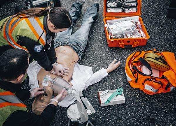 Two paramedics doing CPR demonstration on the ground with a first aid kit.