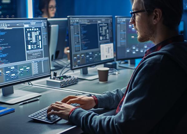 A person sitting at a desk in front of three computer monitors