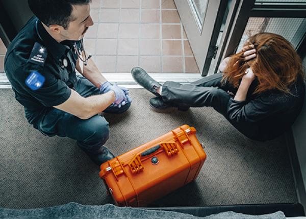 A paramedic checking on a person with an orange first aid kit on the side.