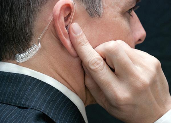 A security officer in a suit wearing earphones, listening to conversations from another officer.