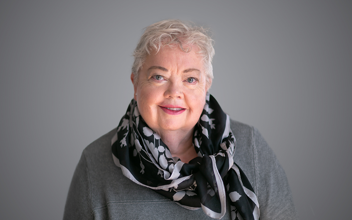 Woman wearing grey top and black patterned scarf.