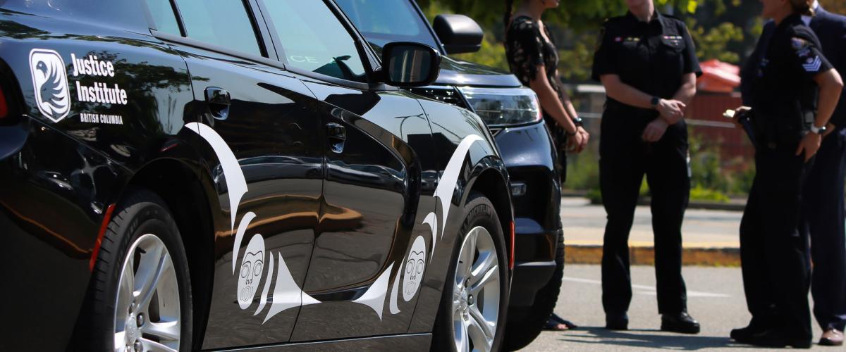 A group of four people stand in front of JIBC Police Academy vehicle with Indigenous artwork on the doors.