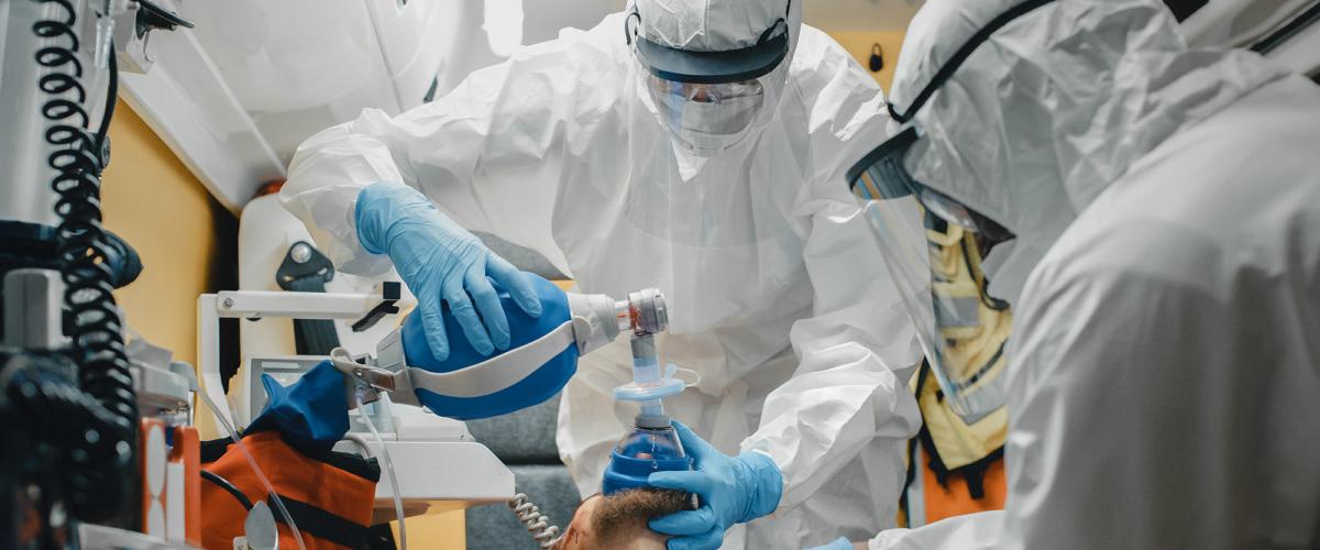 Two paramedics in full personal protective equipment work on a patient in an ambulance.