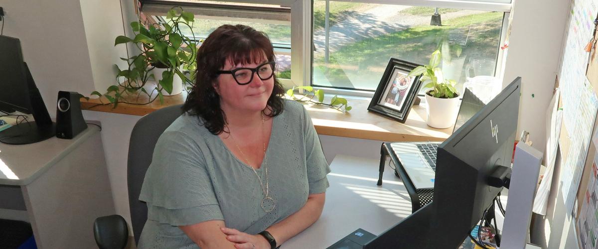 Woman wearing glasses sitting at a desk with hand on mouse looking at computer monitor.