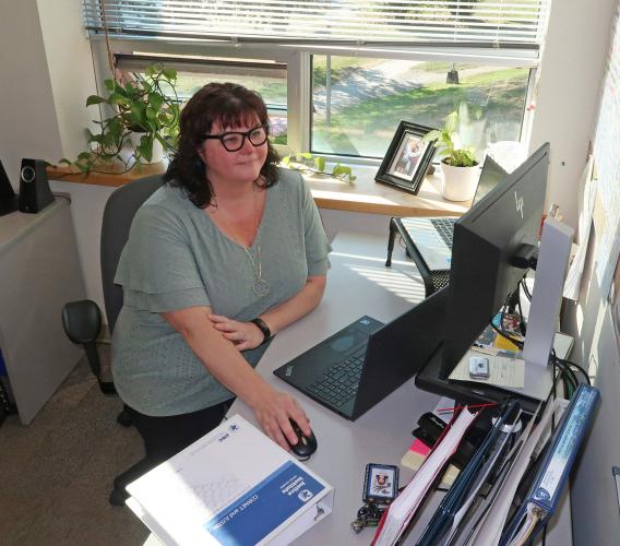 Woman wearing glasses sitting at a desk with hand on mouse looking at computer monitor.