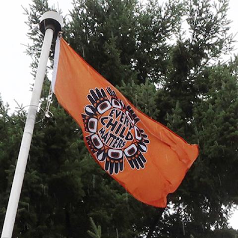 Flagpole flying orange flag with Every Child Matters logo.