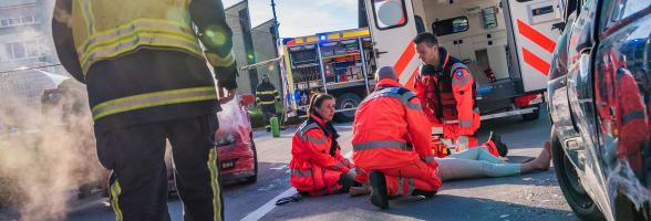 Firefighter walking towards three paramedics treating patient on ground behind ambulance.