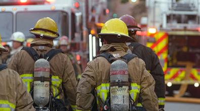 Rear view of firefighters in turnout gear walking towards fire truck..