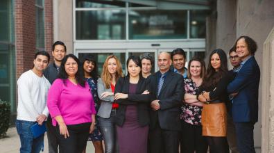 Diverse group of people stand in front of building.