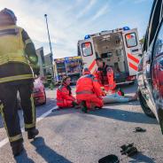 Firefighter walking towards three paramedics treating patient on ground behind ambulance.