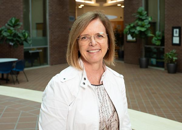 Woman with glasses wearing white jacket and patterned blouse.