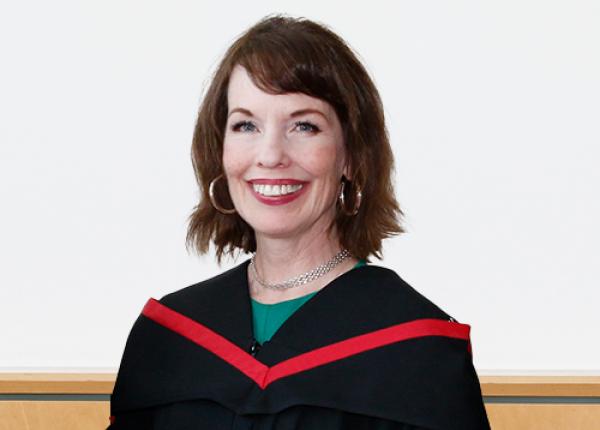 Woman with dark hair wearing black graduation gown with red trim.